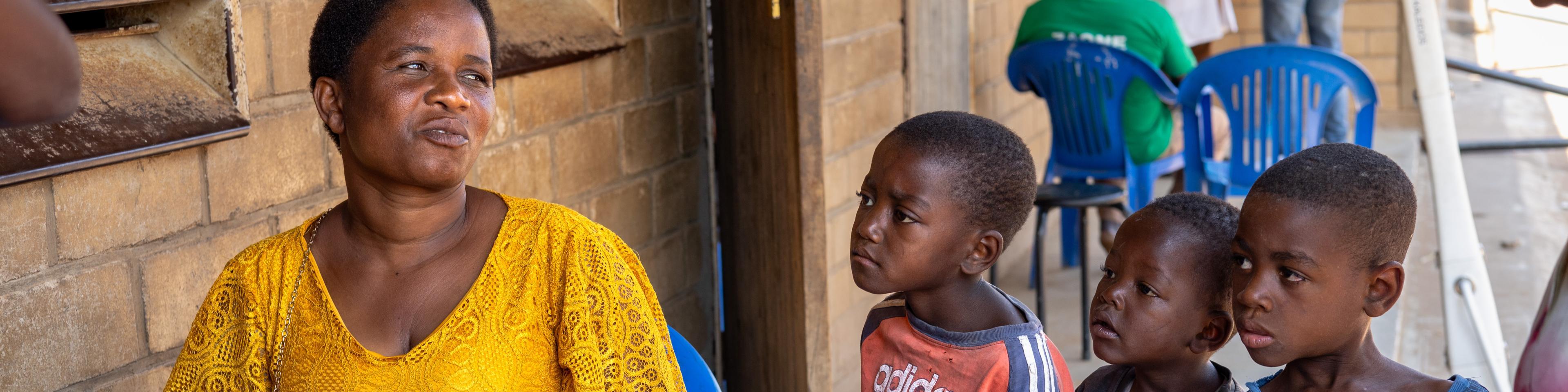 Frau am Brillenverkaufsstand von GoodVision Malawi, beobachtet von neugierigen Kindern