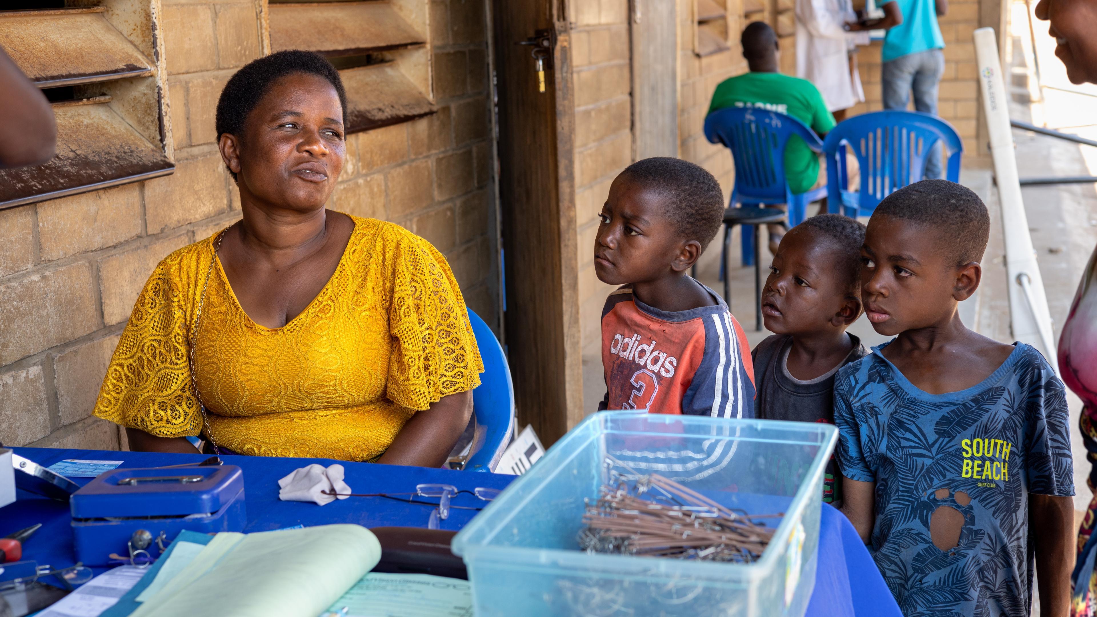 Frau am Brillenverkaufsstand von GoodVision Malawi, beobachtet von neugierigen Kindern