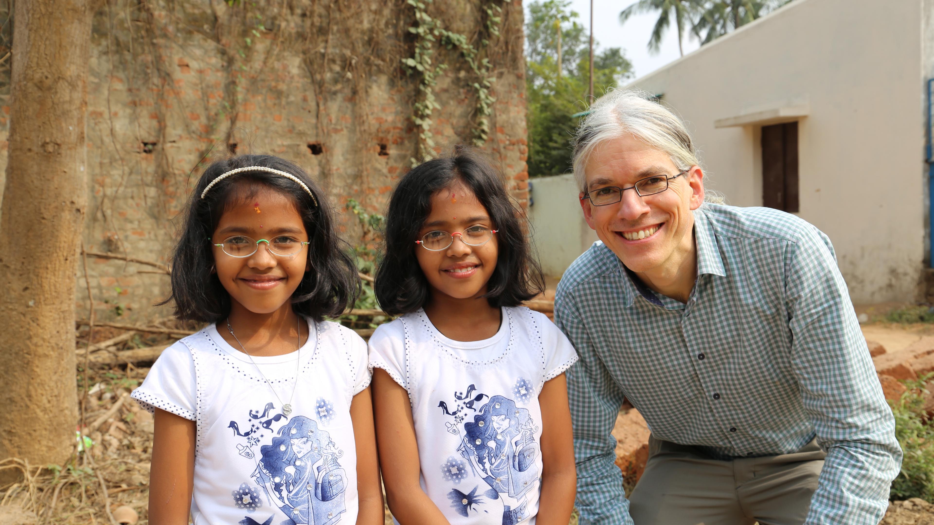 Martin Aufmuth neben Zwillingsmädchen in Indien, die Mädchen tragen EinDollarBrillen