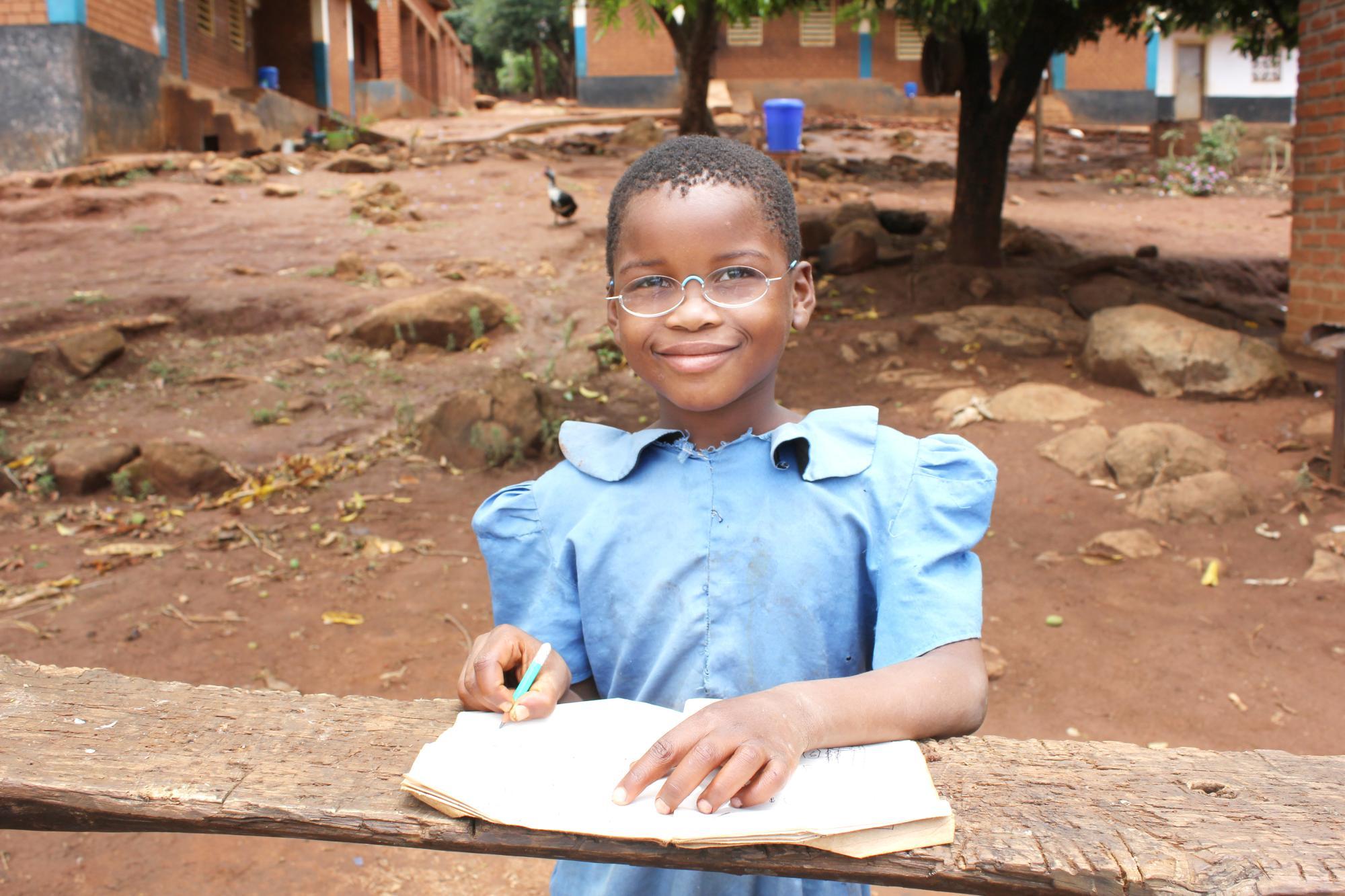 Schülerin aus Malawi, mit Schulheft und Stift, trägt EinDollarBrille