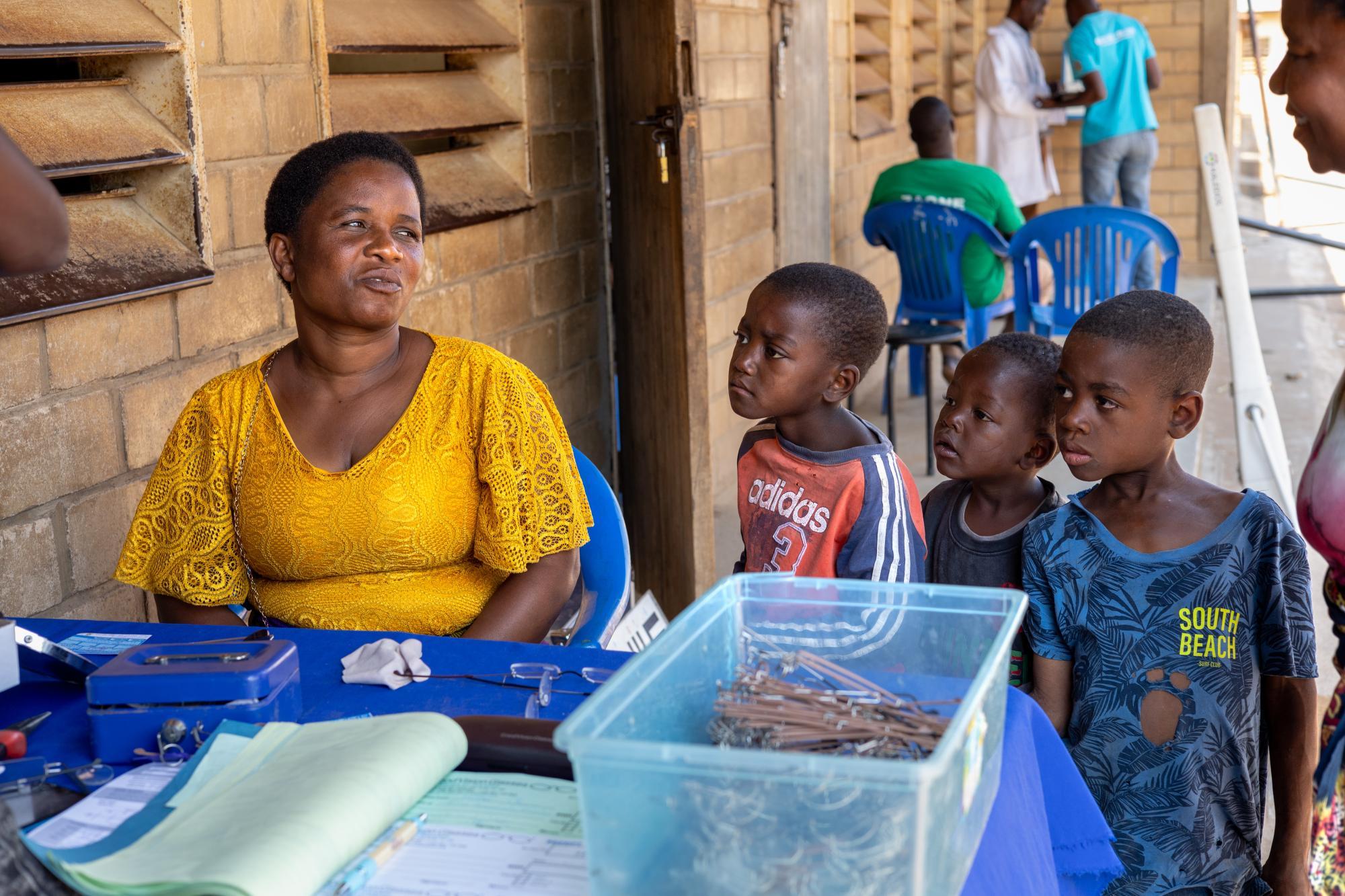 Frau am Brillenverkaufsstand von GoodVision Malawi, beobachtet von neugierigen Kindern